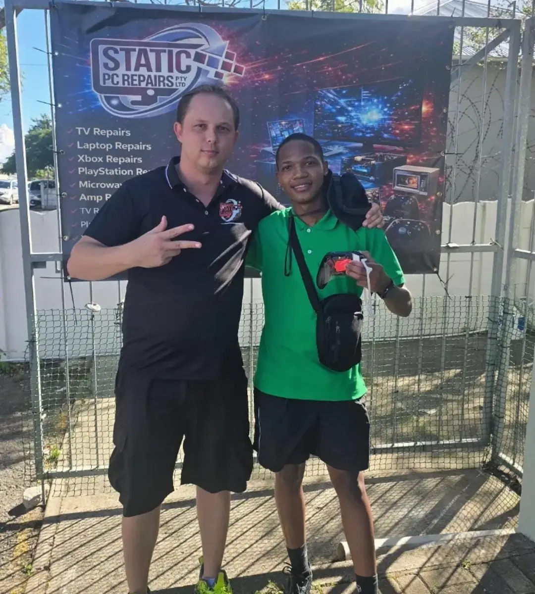 Tim Kramm in a black Static PC Repairs shirt with a customer holding his controller, in front of the shop's banner